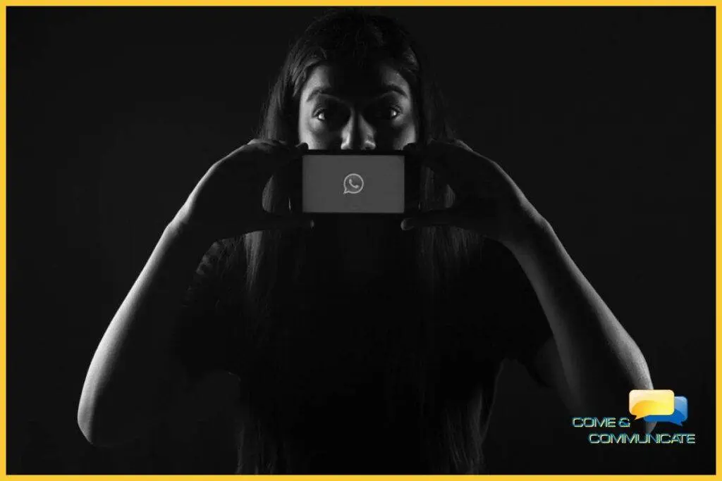 Una mujer tapando su boca con un teléfono móvil donde se ve el símbolo de Whatsapp