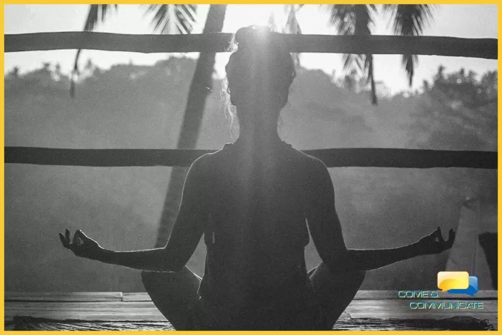 Contraluz de una chica meditando de cara al sol con los codos apoyados sobre sus rodillas