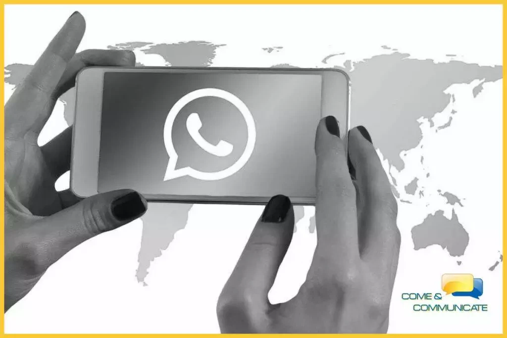 Manos de una mujer sujetando un móvil y un mapamundi de fondo, viendo cómo utilizar WhatsApp para vender.