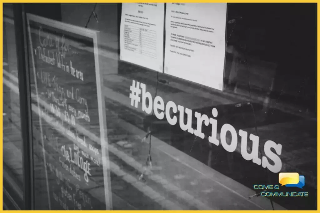Frase #becurious puesta en vinilo en la ventana de un local junto con una pizarra negra.