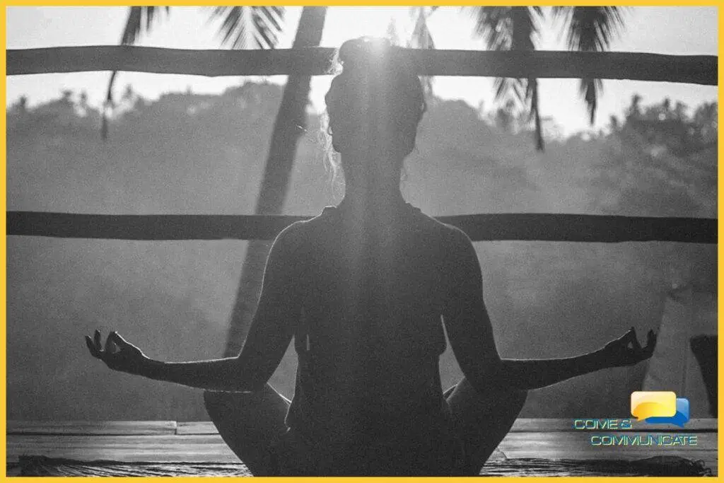 Contraluz de una chica meditando de cara al sol con los codos apoyados sobre sus rodillas