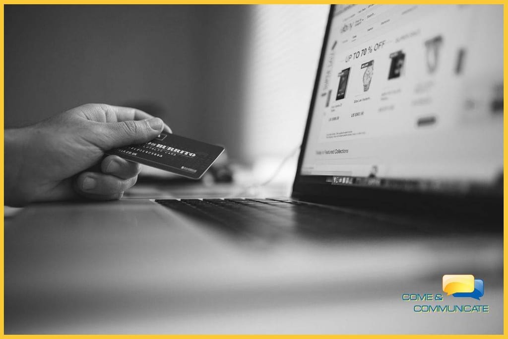 Mano sujetando una tarjeta de crédito con el portátil al lado para realizar una compra online