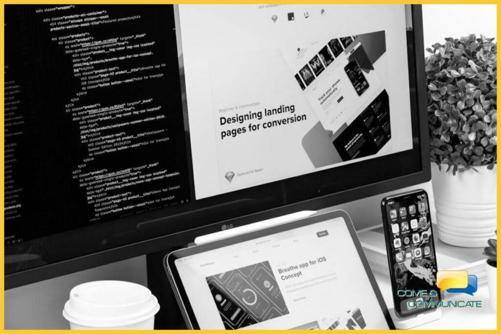 Un escritorio de trabajo que muestra el proceso de diseño y desarrollo digital. Un monitor muestra código HTML y el diseño de una landing page, mientras una tablet y un smartphone en primer plano muestran los 'wireframes' y el concepto de una app. Esta configuración ilustra el trabajo detrás de una aplicación móvil para tu negocio.