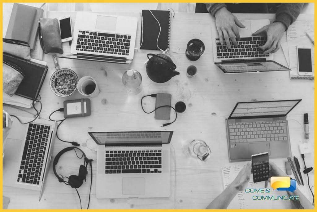 Equipo de trabajo digital investigando fuentes de contenido para empresas con portátiles y dispositivos en Come & Communicate.